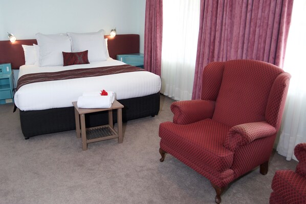 Une chambre d’hôtel avec un grand lit, un fauteuil rouge, une petite table et une table de chevet.