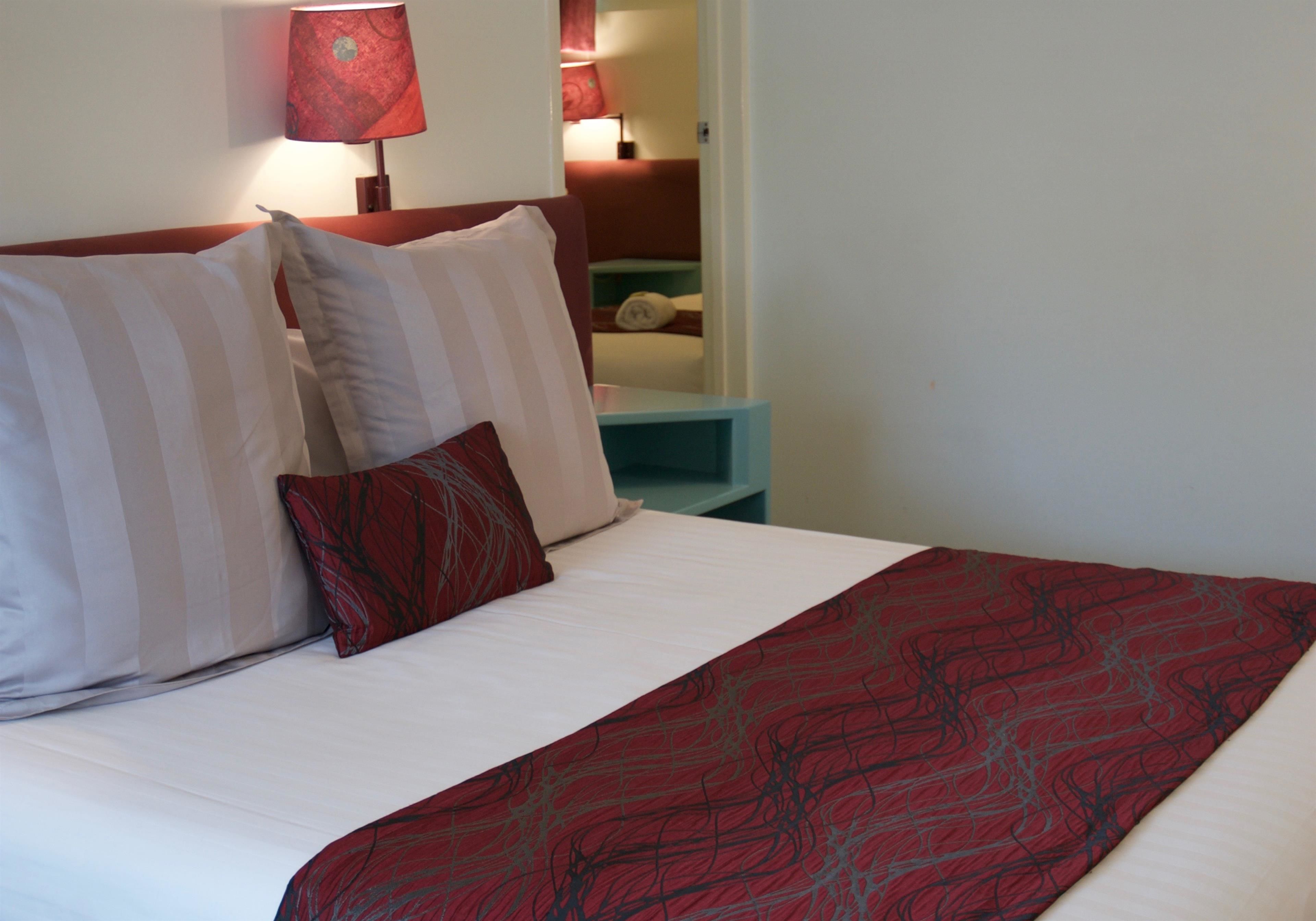 Una cama bien hecha con almohadillas a rayas y una colcha estampada en rojo.