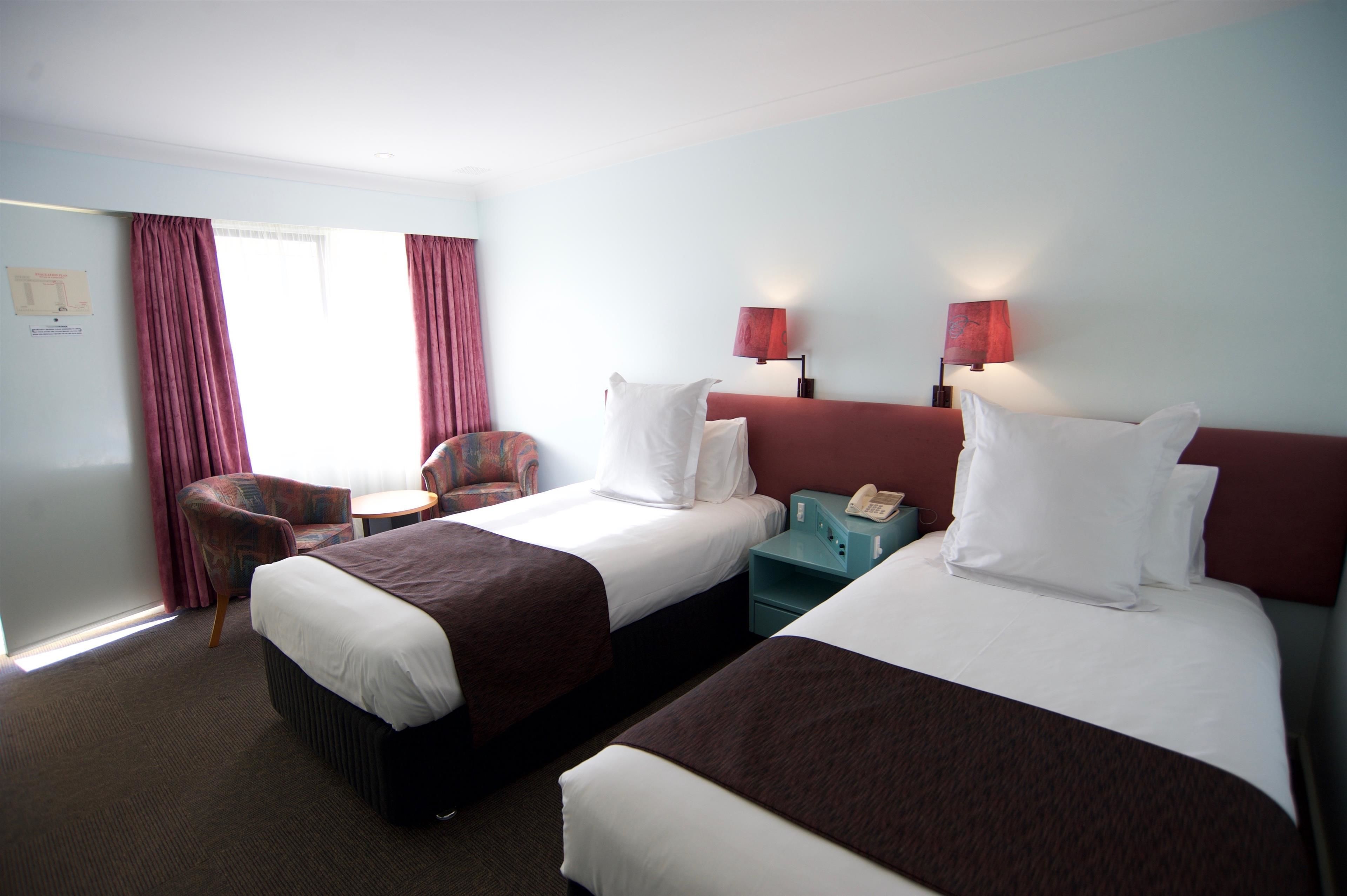 Ein Hotelzimmer mit zwei Betten, einem Sessel, einem kleinen Tisch und einem Nachttisch mit Telefon.
