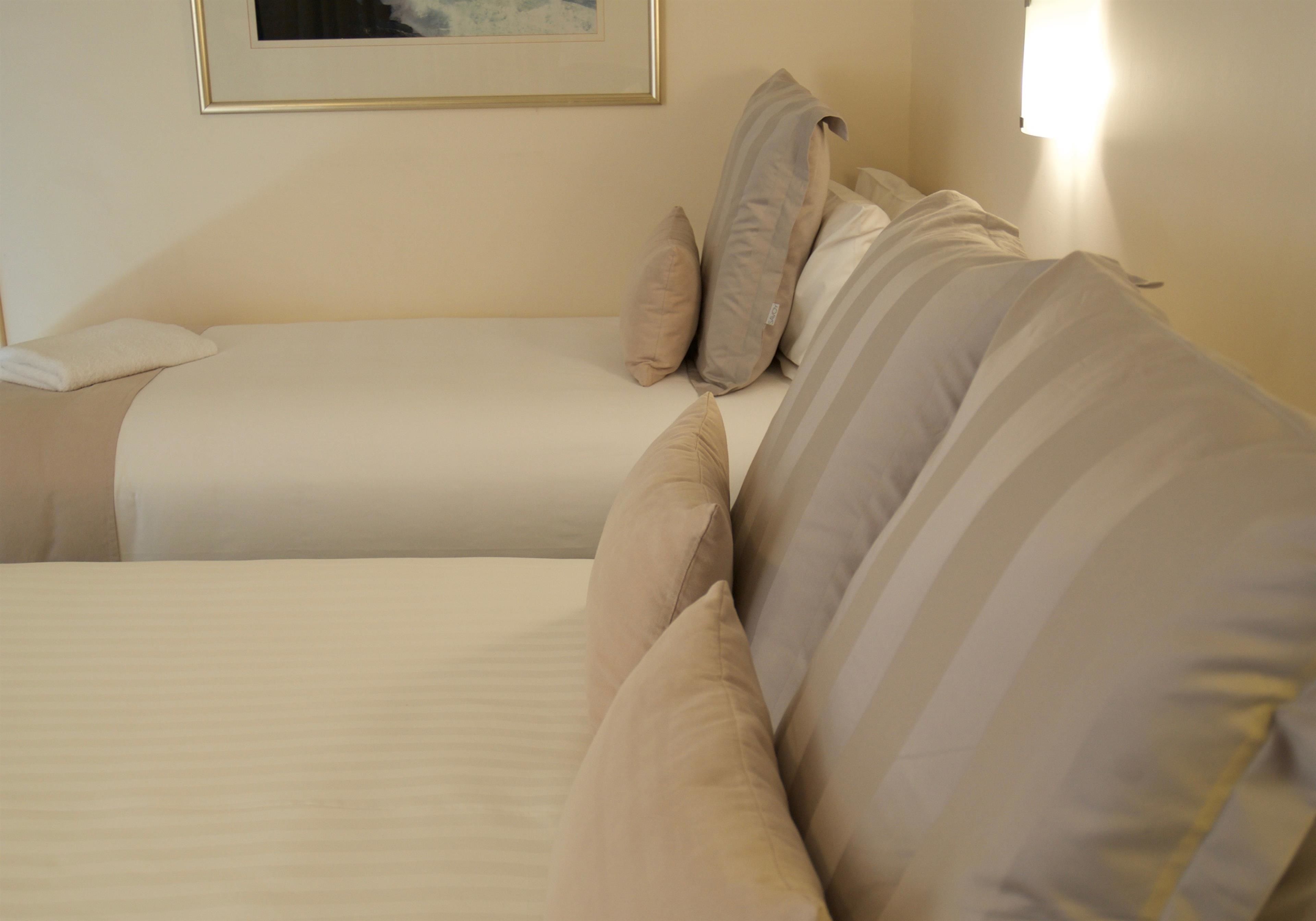 A hotel room with two beds, each with a striped pillow and a white blanket.