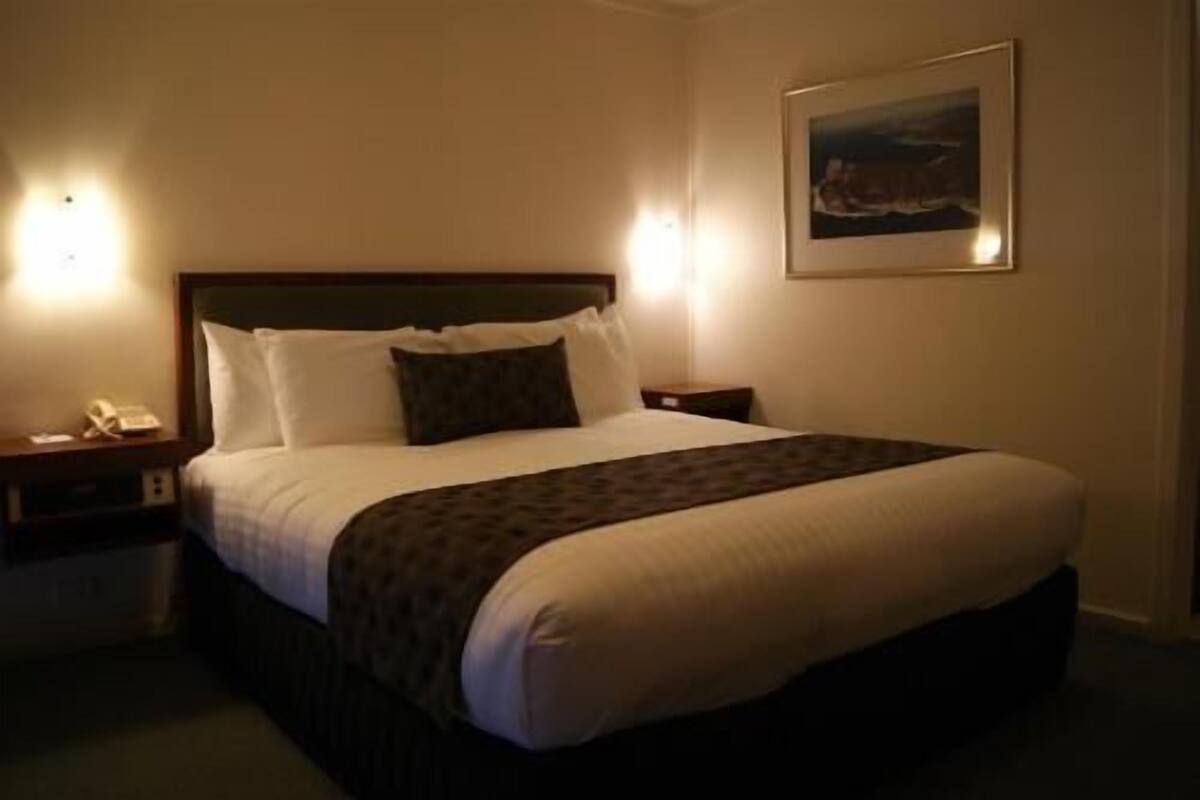 A hotel room with a large bed, bedside tables, a wall-mounted telephone, and a framed picture.