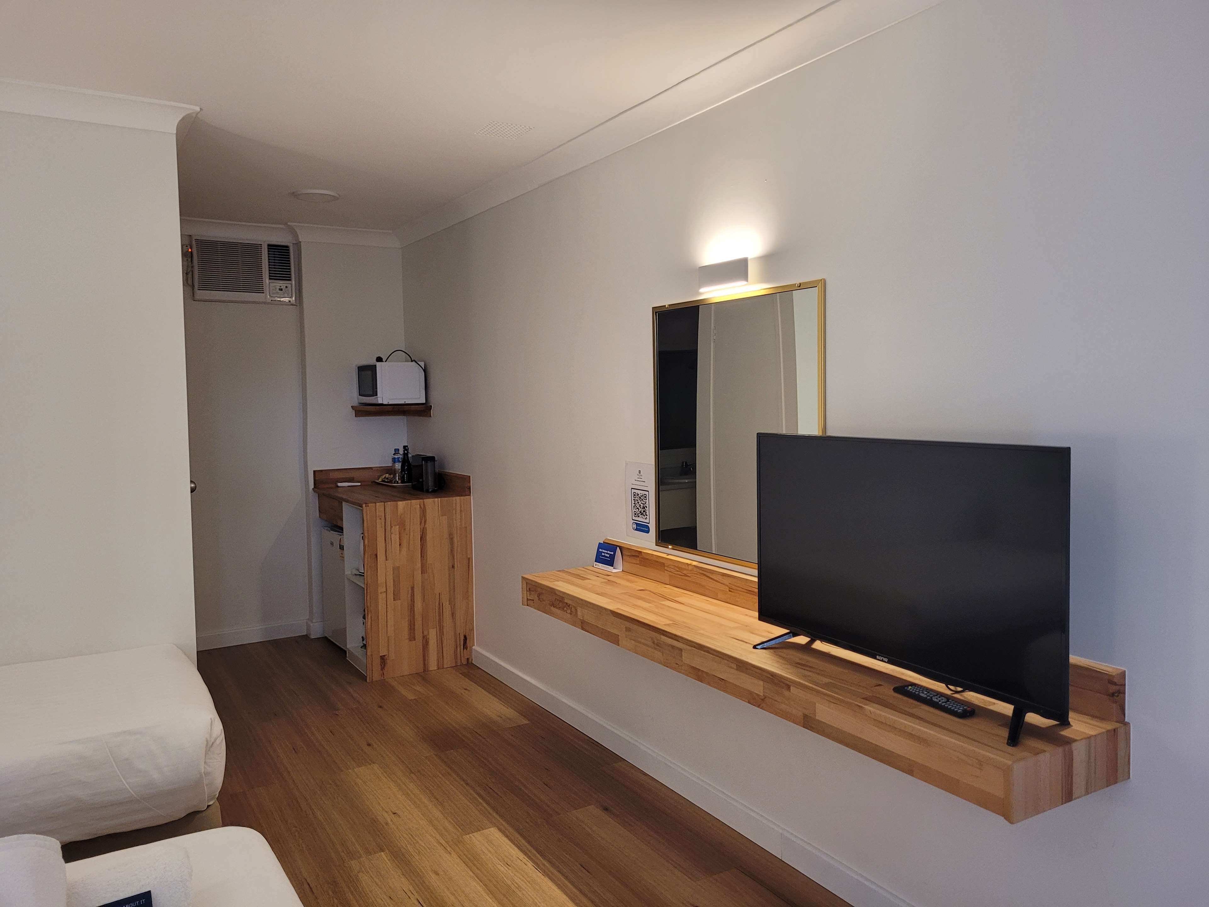 Een compacte kamer met een houten opbergmeubel, een wandgemonteerde televisie en een spiegel.