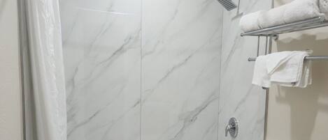 Un baño moderno con pared de ducha de mármol, una bañera, un inodoro y un lavabo.