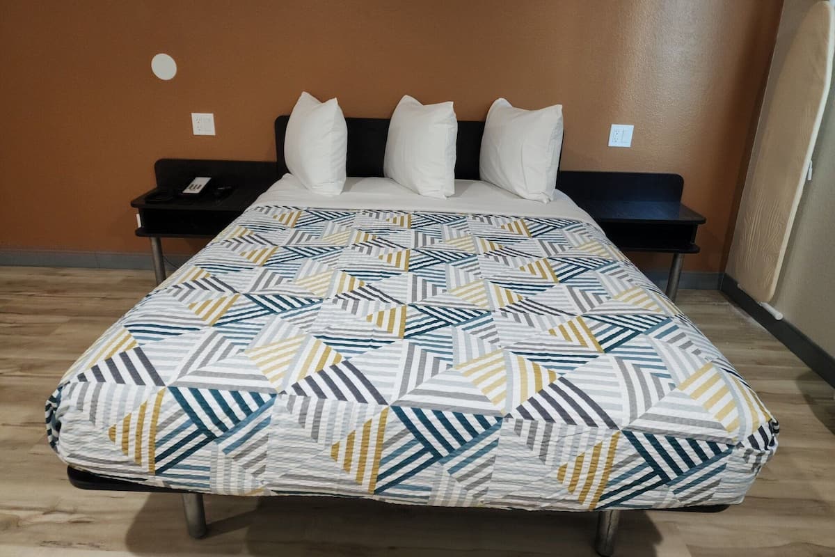 A hotel room with a bed, a nightstand, and a wall socket.