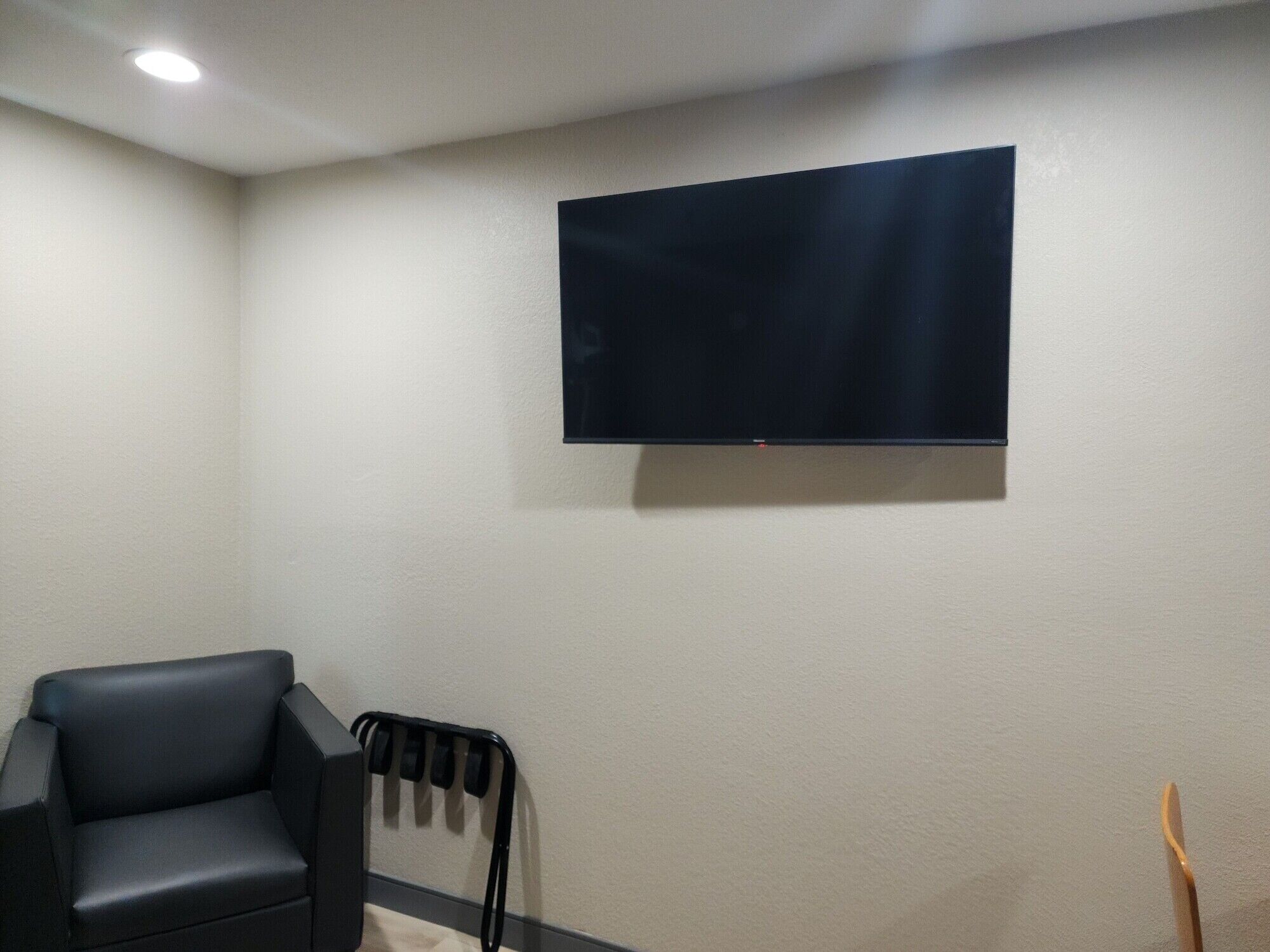 A room with a flat-screen TV mounted on the wall, a black leather chair, and a black radiator.