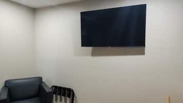 A room with a flat-screen TV mounted on the wall, a black leather chair, and a black radiator.