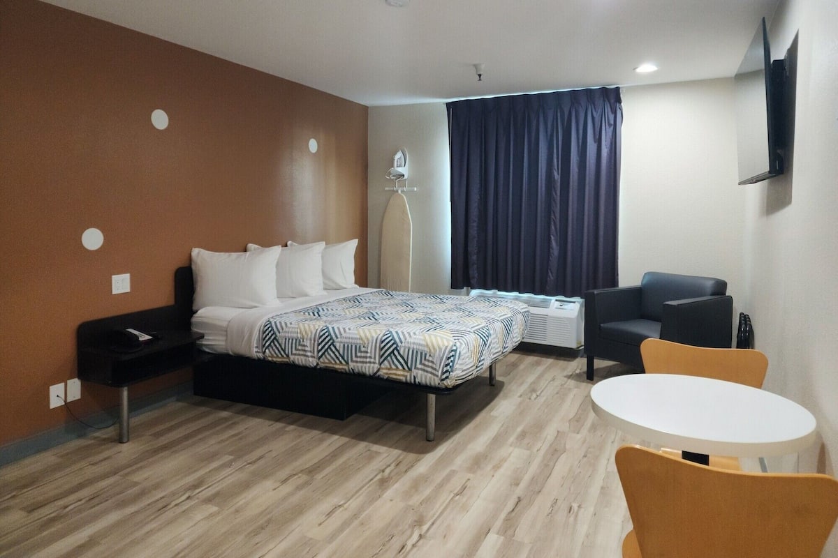 A hotel room with a bed, a desk, a chair, a table, and a TV mounted on the wall.