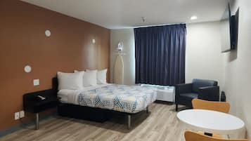 Une chambre d’hôtel équipée d’un lit, d’un bureau, d’une chaise, d’une table et d’un téléviseur fixé au mur.