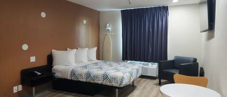 A hotel room with a bed, a desk, a chair, a table, and a TV mounted on the wall.