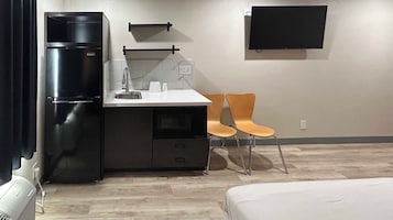 Una habitación de hotel compacta con kitchenette, una cama, un televisor y dos sillas.