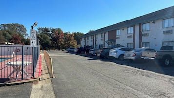 A parking lot with a speed limit sign, a fenced pool area, and a row of parked cars.