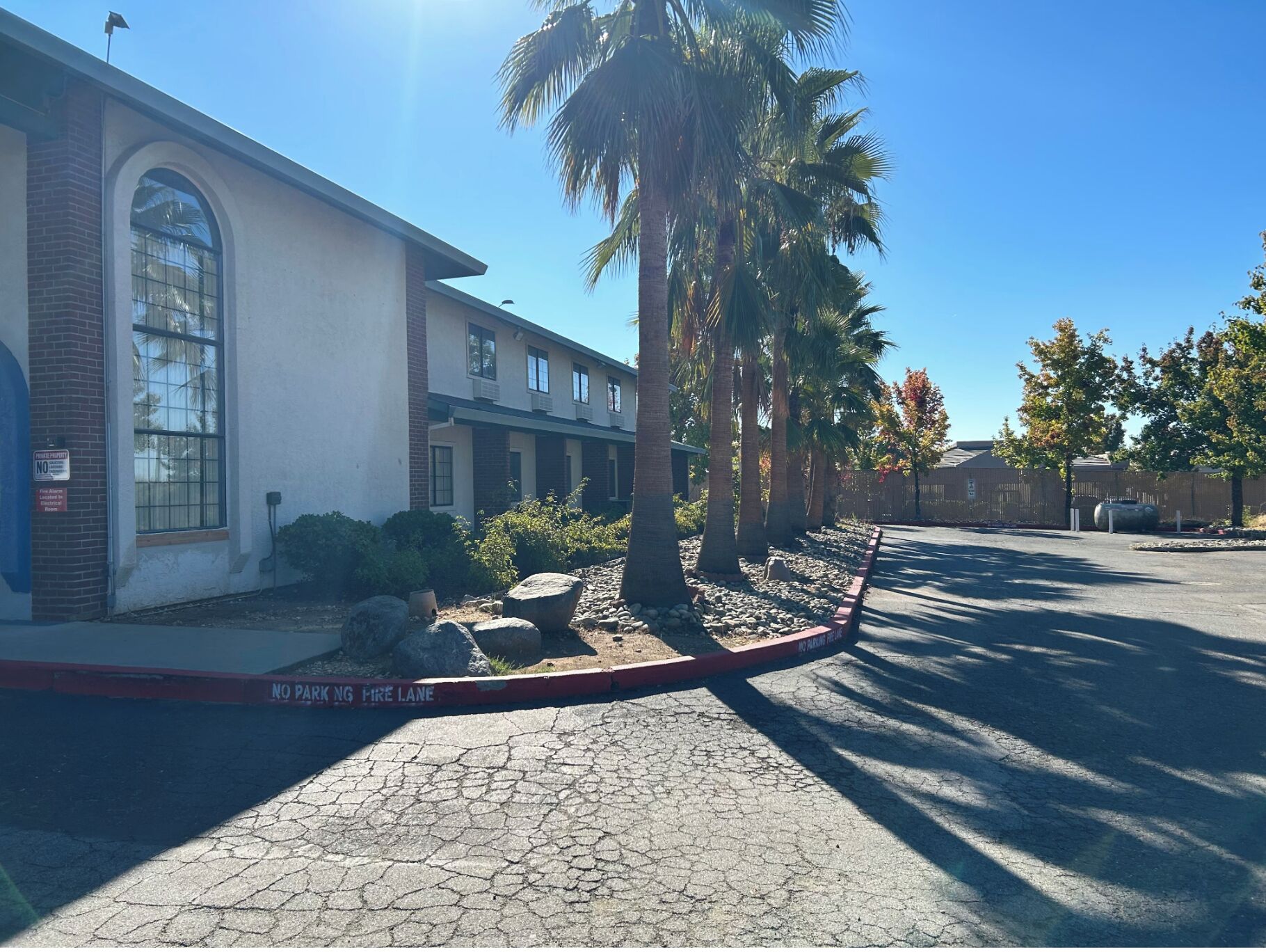 A building with a large arched window, a fire lane, and palm trees.