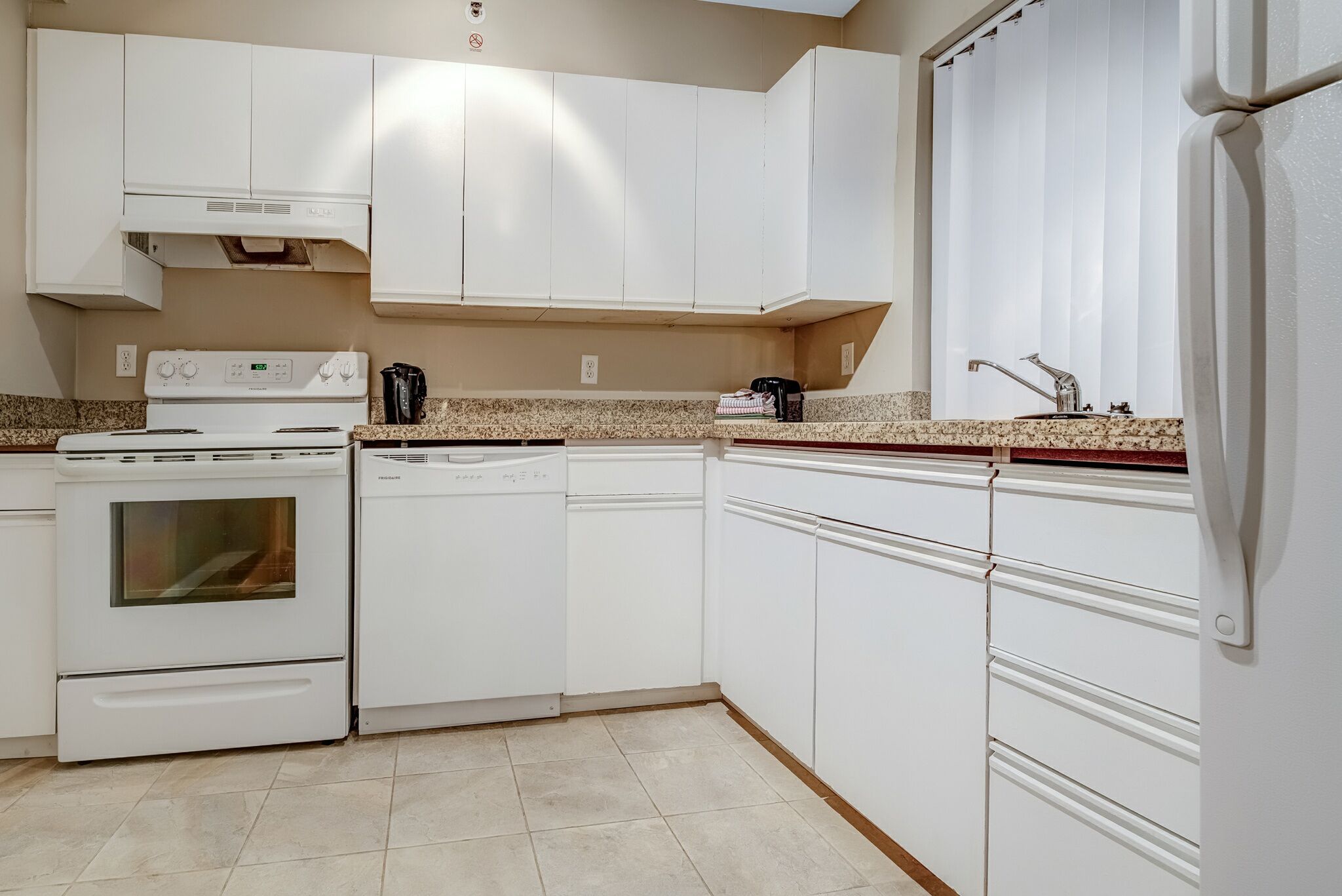 Une cuisine avec des meubles blancs, une cuisinière, un lave-vaisselle et un évier.
