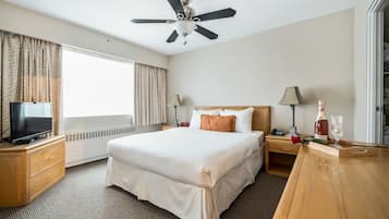 A hotel room with a large bed, a ceiling fan, a TV on a wooden dresser, and a window with curtains.