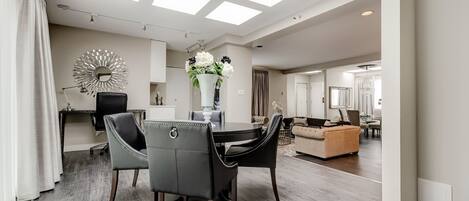 A modern living room with a dining area, featuring a skylight, a round mirror, and a vase with flowers.