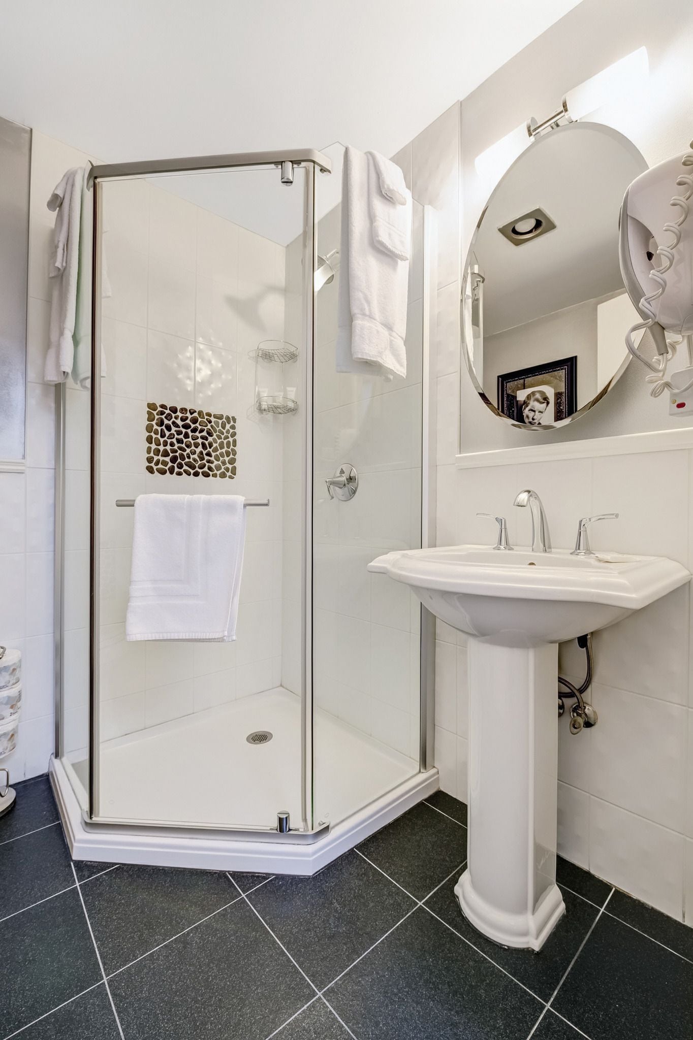 A modern bathroom with a glass shower enclosure, a pedestal sink, and a large mirror.