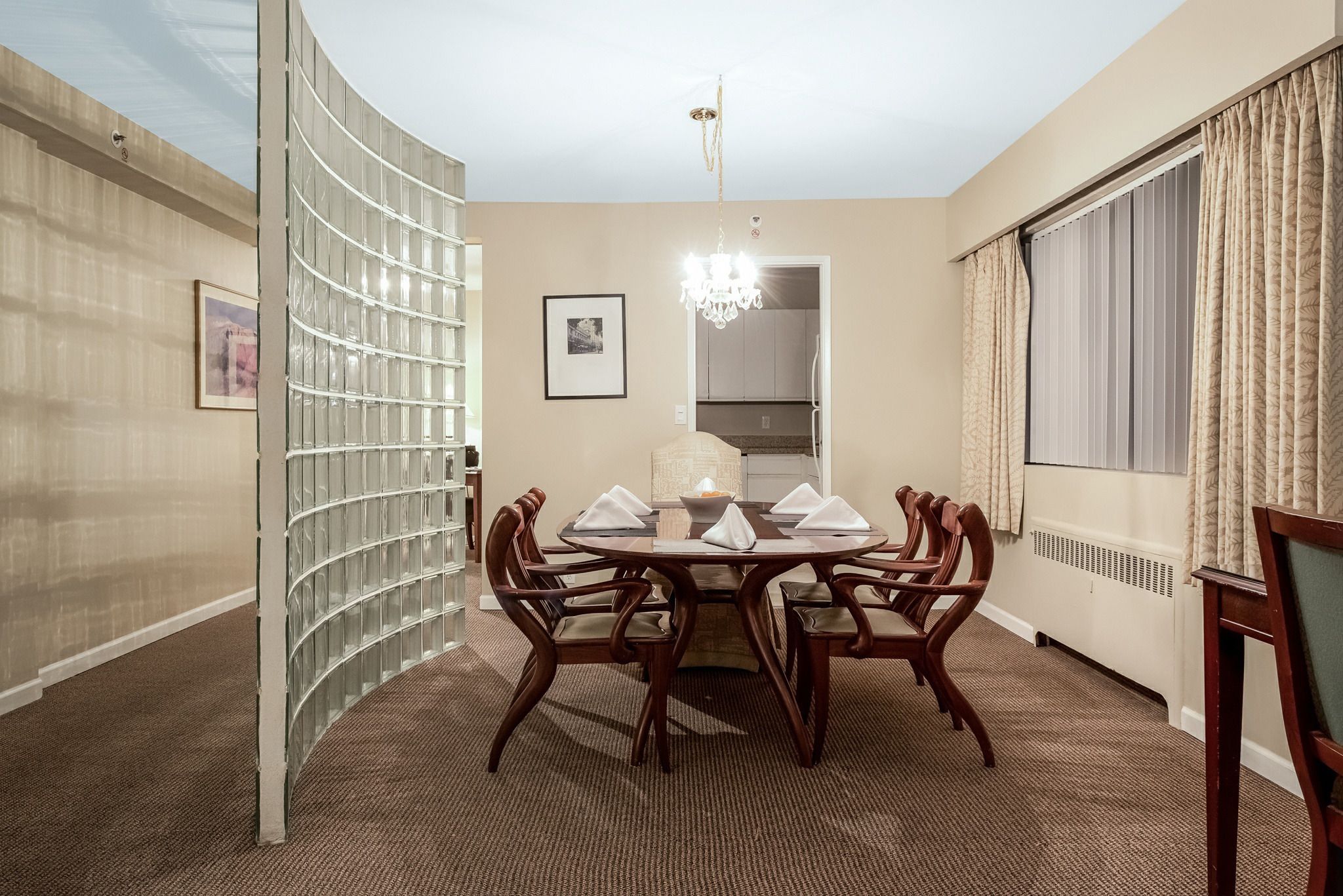 Quarto de hotel com uma mesa de jantar redonda posta para quatro pessoas, um candelabro e uma grande janela com cortinas.