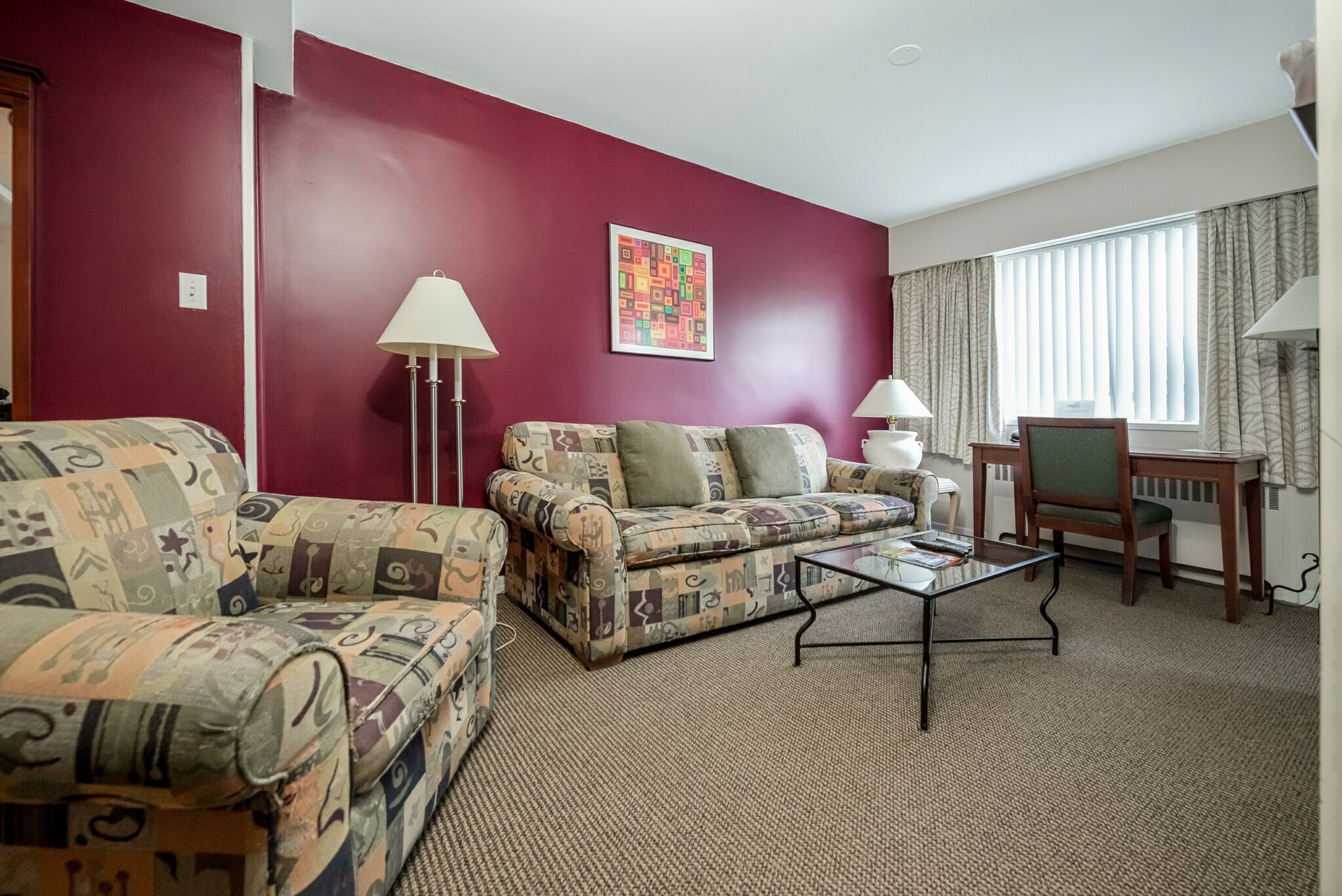 Ein Wohnzimmer mit roter Wand, zwei gestreiften Sofas, einem Glastisch, einer Lampe und einem Sessel.