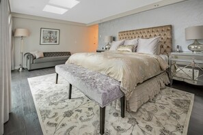 Een slaapkamer met een groot bed, een bankje, een sofa en een nachtkastje.