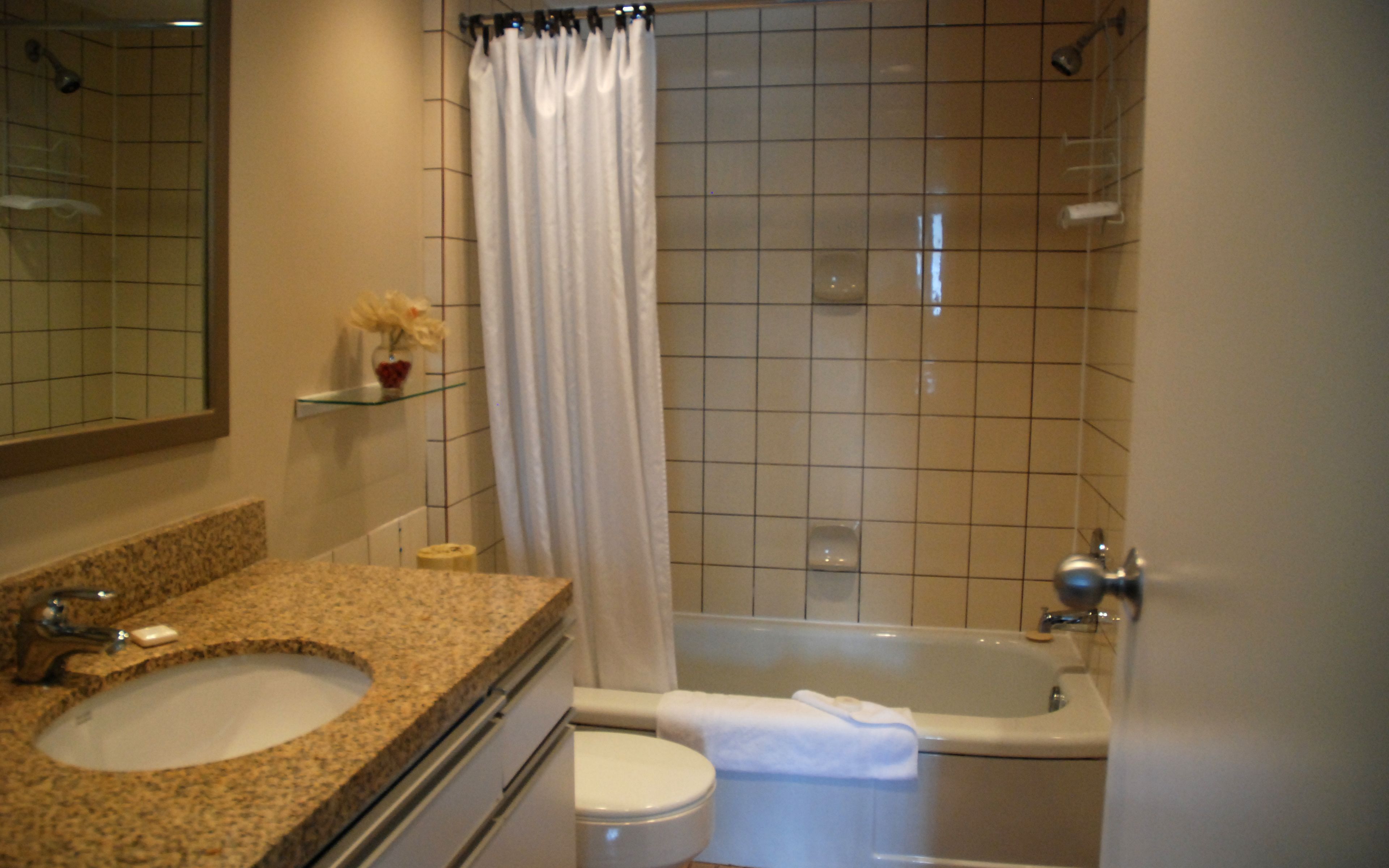 Un baño con lavamanos de encimera de granito, inodoro, bañera y cortina de ducha.