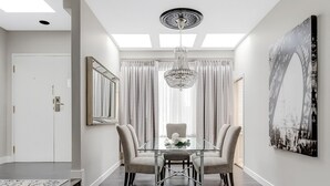Un coin repas avec une table en verre, quatre chaises, un lustre et un grand tableau encadré au mur.