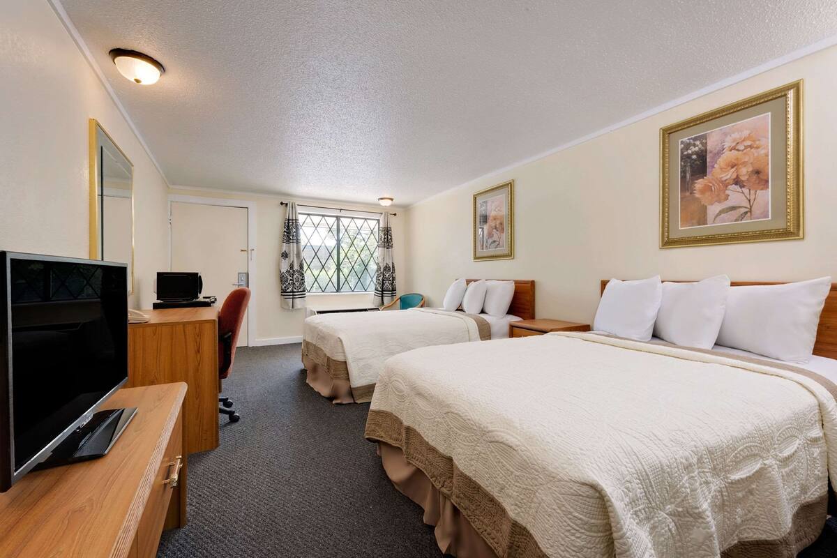 A hotel room with two beds, a desk with a TV, a chair, and a door leading to a balcony.