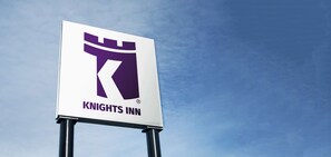 A Knights Inn sign with a knight's helmet and sword logo, mounted on a metal pole against a clear sky.