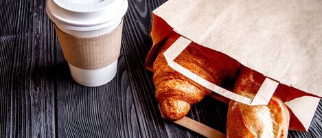 A coffee cup and a paper bag with bread on a wooden surface.