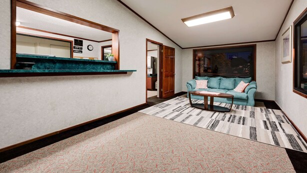 A modern living room with a teal sofa, a coffee table, a large mirror, and a view of the outdoors. - Knights Inn Macedonia (Macedonia)