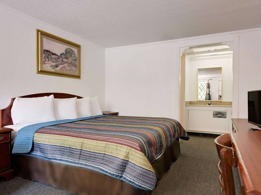A hotel room with a bed, a wooden nightstand, a desk, a television, and a mirror.