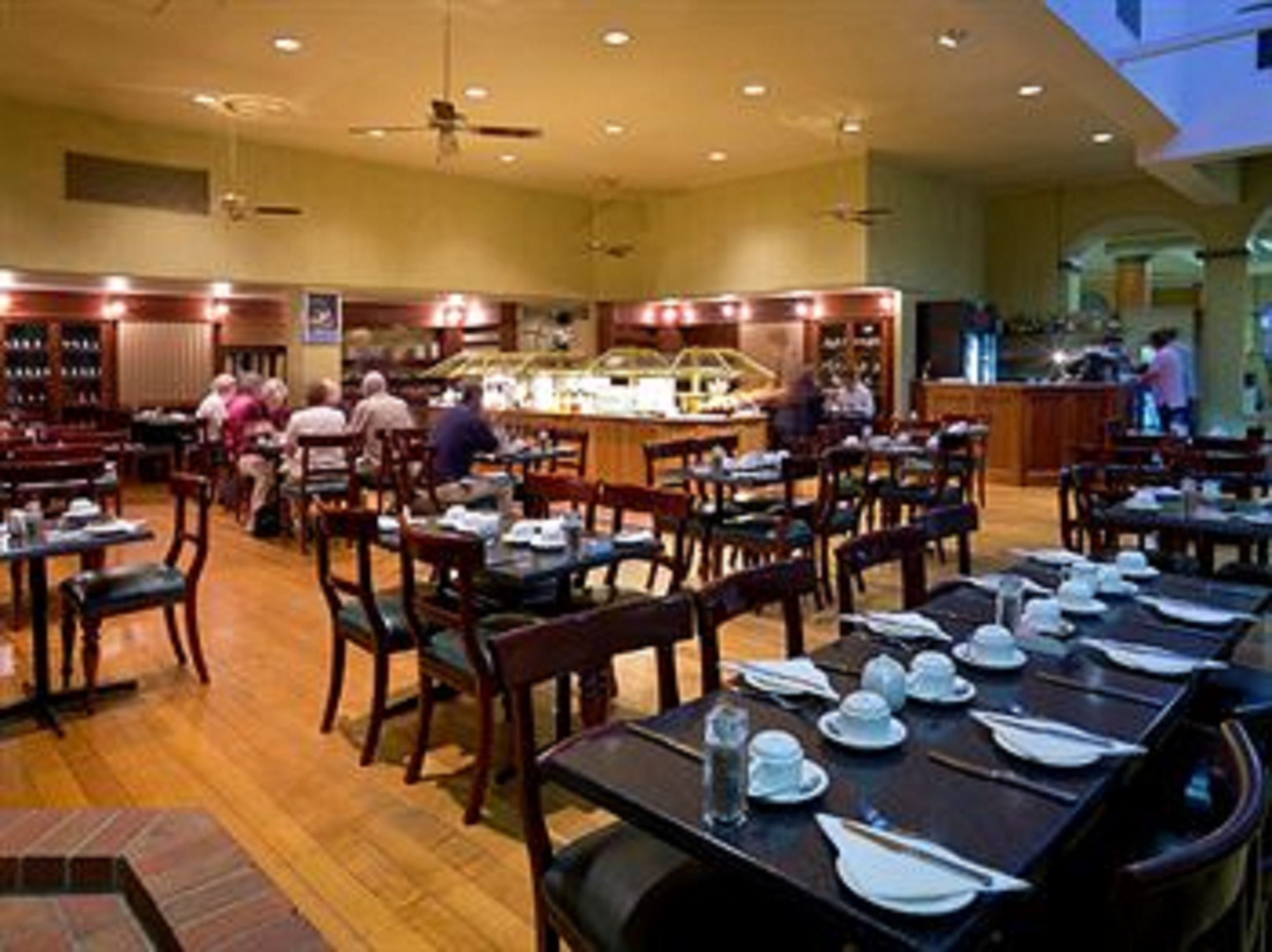 A restaurant with wooden tables and chairs, a bar area, and a ceiling fan.