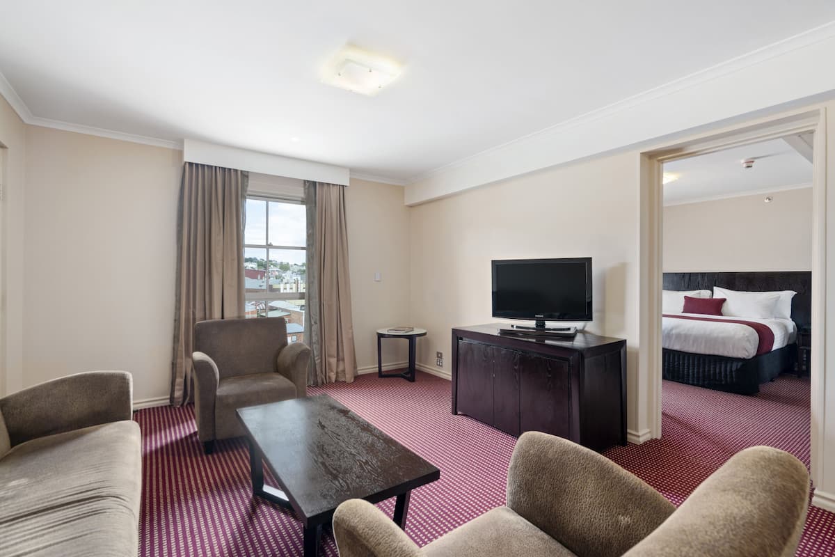 A hotel room with a large bed, a TV, a desk, and a sofa.