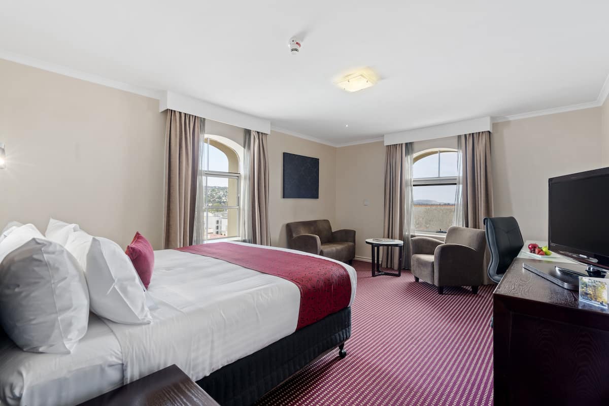 A hotel room with a large bed, two armchairs, a desk with a TV, and a small table.