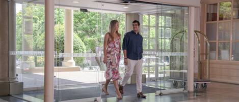 Una entrada de hotel moderna con puertas de vidrio, vista despejada al exterior y rampa accesible para sillas de ruedas.