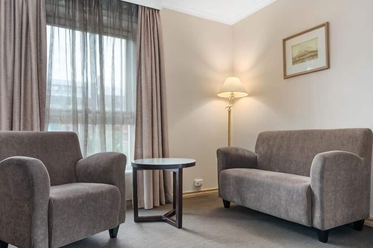 A hotel room with two armchairs, a small round table, a floor lamp, and a framed picture on the wall.