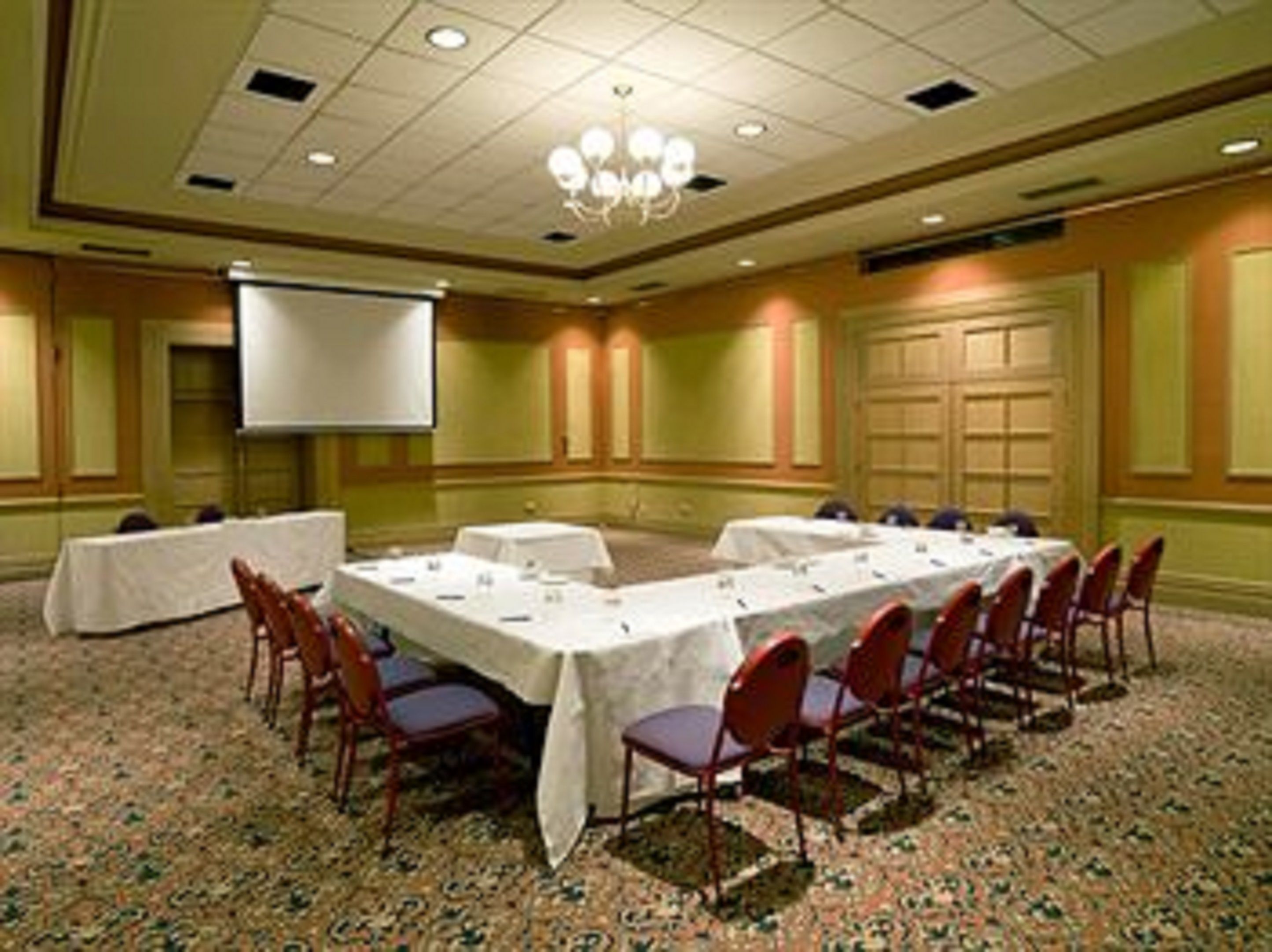 A conference room with a long table, chairs, a projector screen, and a carpeted floor.