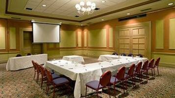 A conference room with a long table, chairs, a projector screen, and a carpeted floor.
