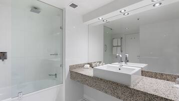 Une salle de bain moderne dotée d’une douche à parois de verre, d’un comptoir en granit et d’un grand miroir.
