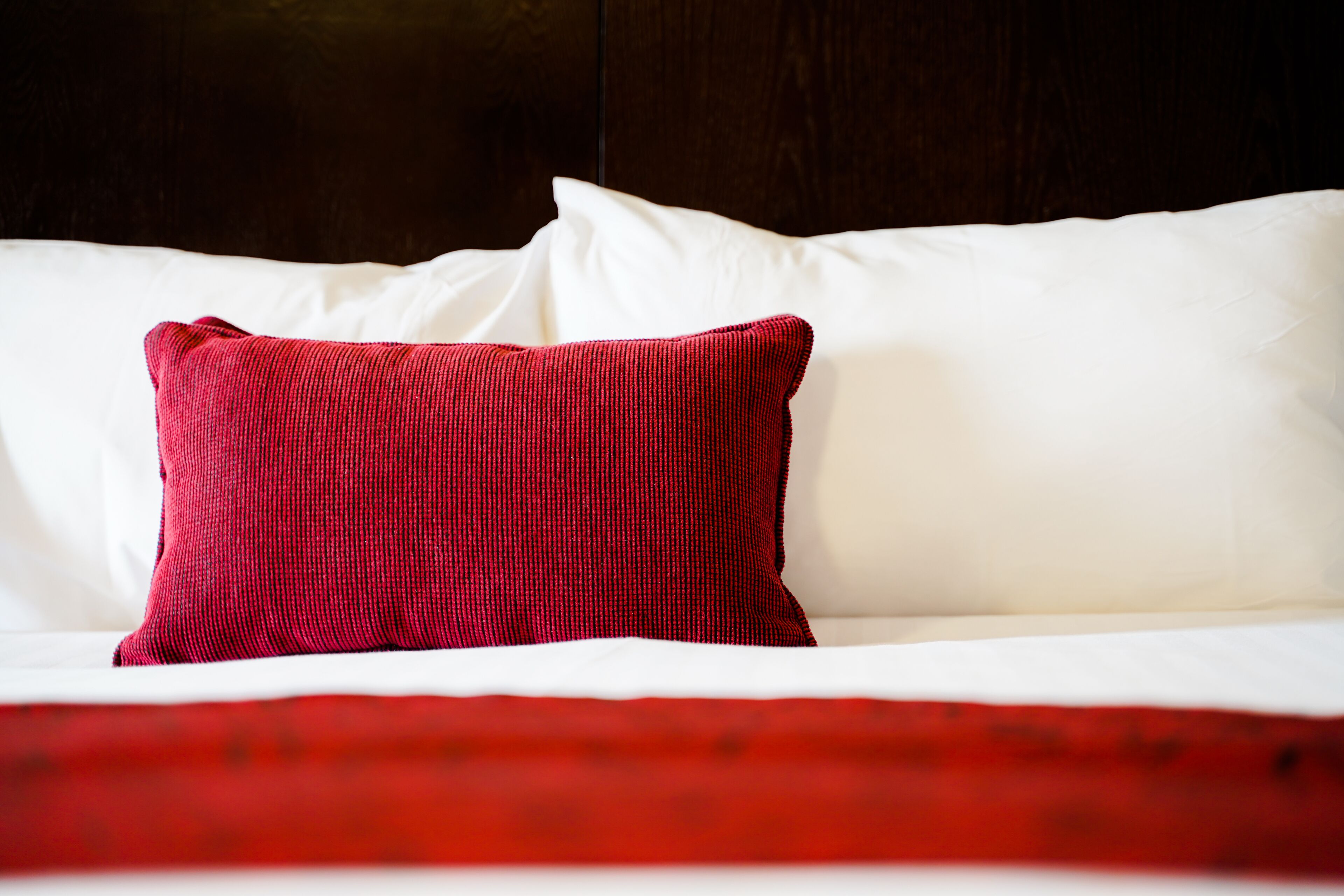 Een bed met witte lakens en een rood kussen.