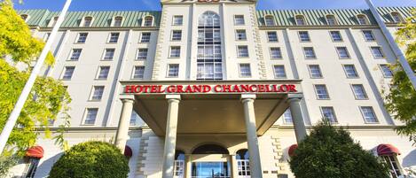 A large, historic building with a grand entrance, columns, and a prominent sign reading "HOTEL GRAND CHANCELLOR."