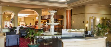 A hotel lobby with a reception desk, seating area, and a fountain.