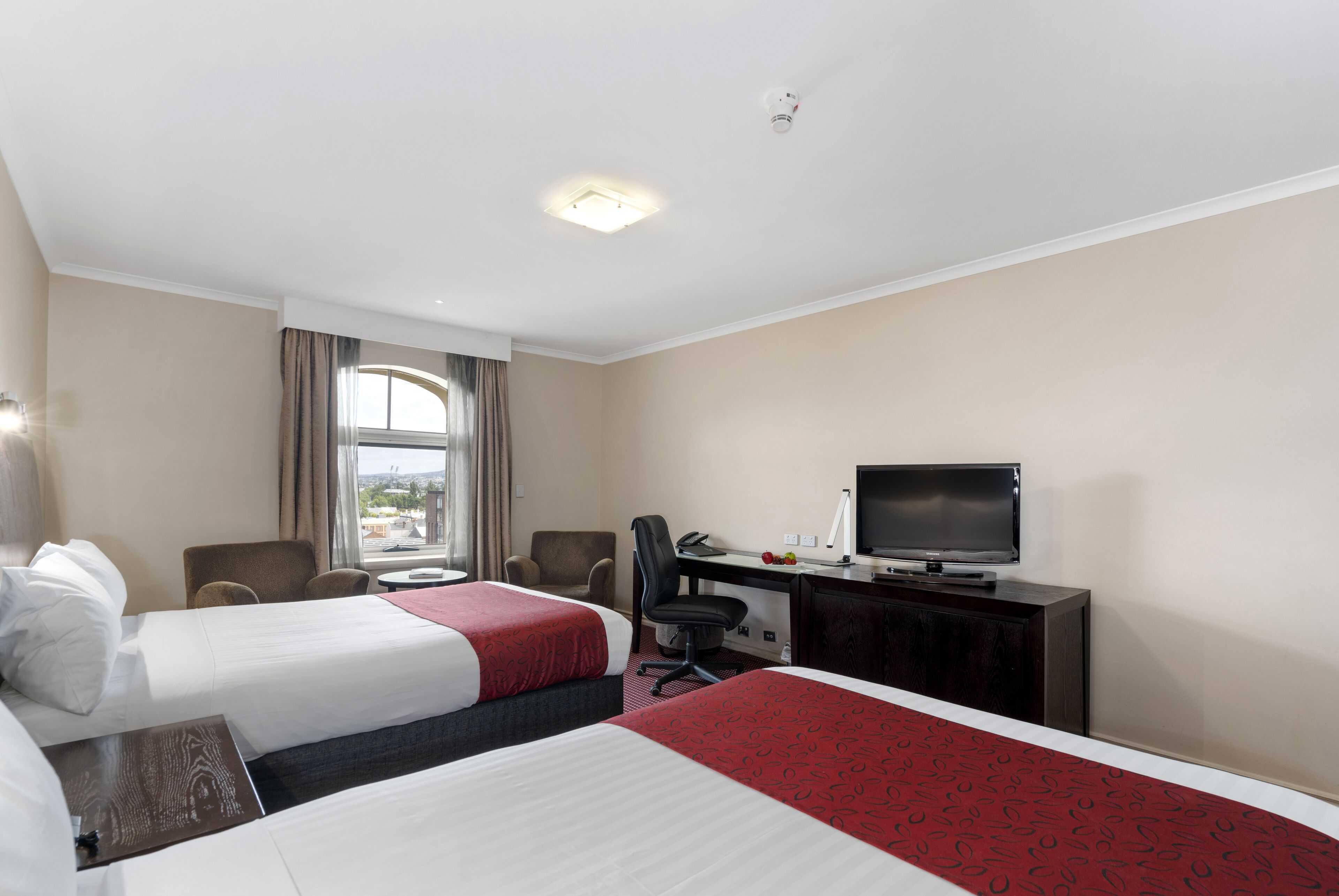 A hotel room with two beds, a desk with a television, a chair, and a window with curtains.