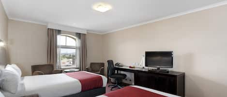 A hotel room with two beds, a desk with a television, a chair, and a window with curtains.