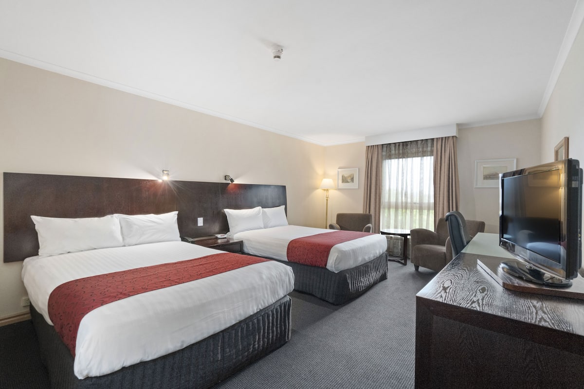 A hotel room with two beds, a desk, a chair, a television, and a lamp.