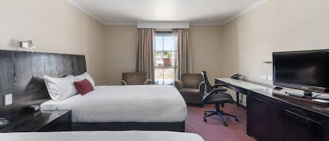Habitación de hotel con dos camas, un escritorio con televisor, una silla y vistas al exterior.