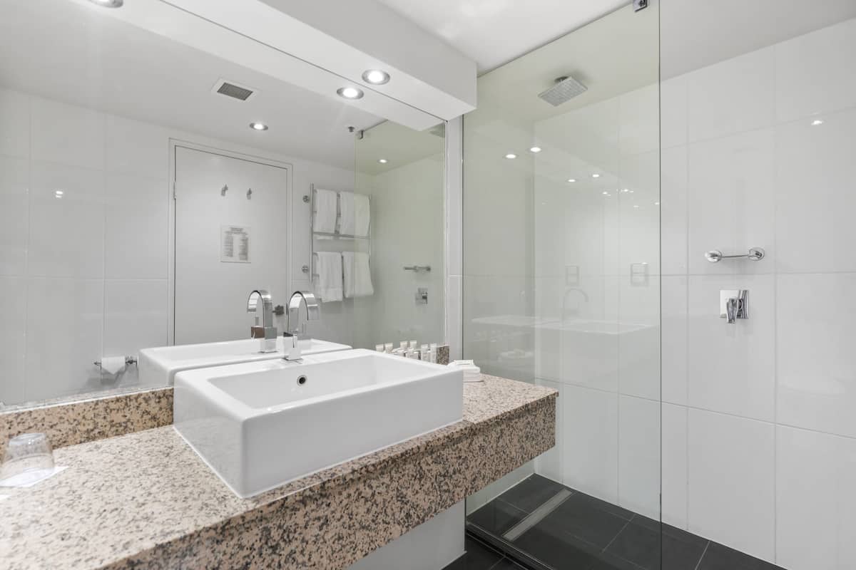 A modern bathroom with a large white sink, a glass shower enclosure, and a granite countertop.