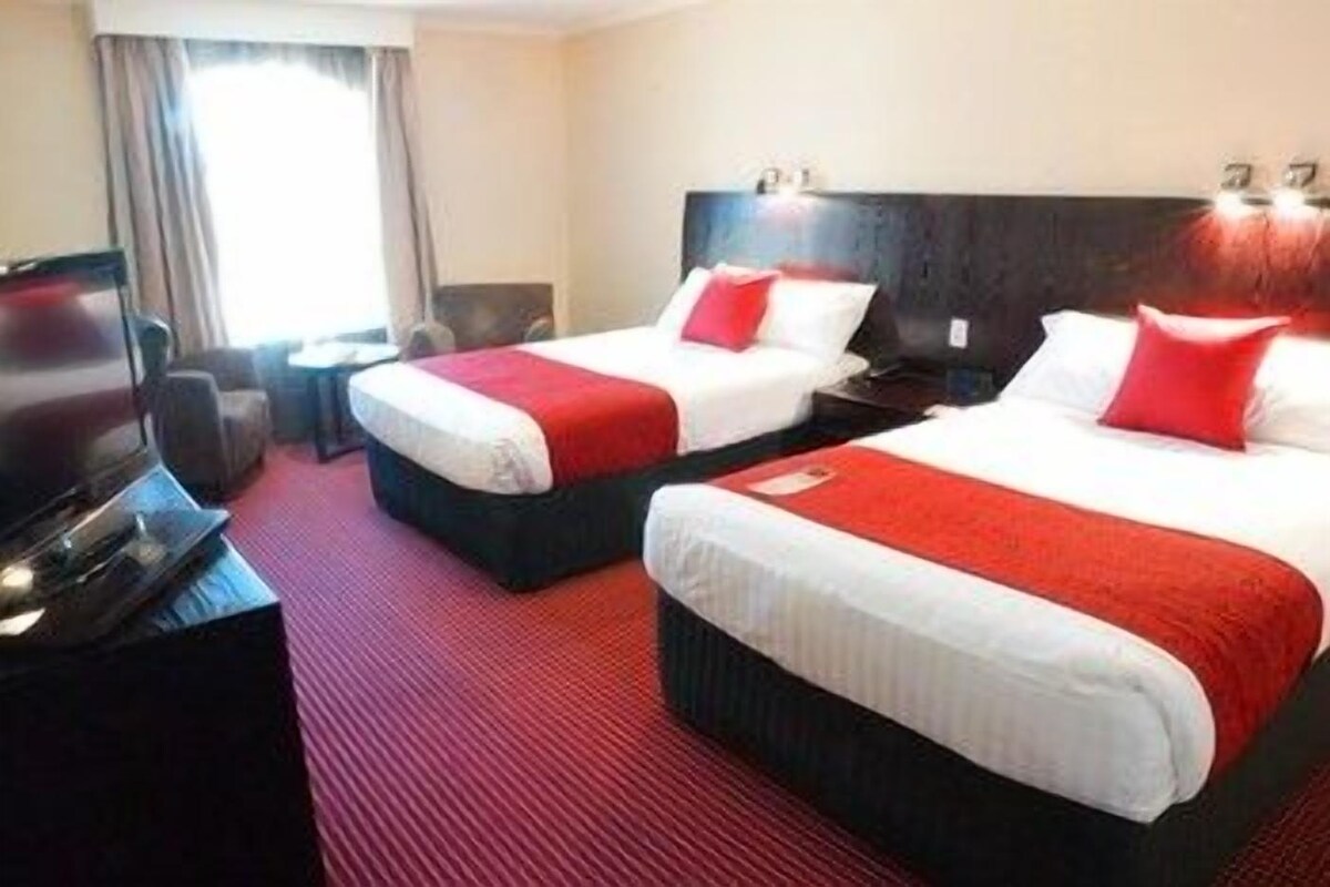 Habitación de hotel con dos camas, televisión, escritorio y ventana con cortinas.