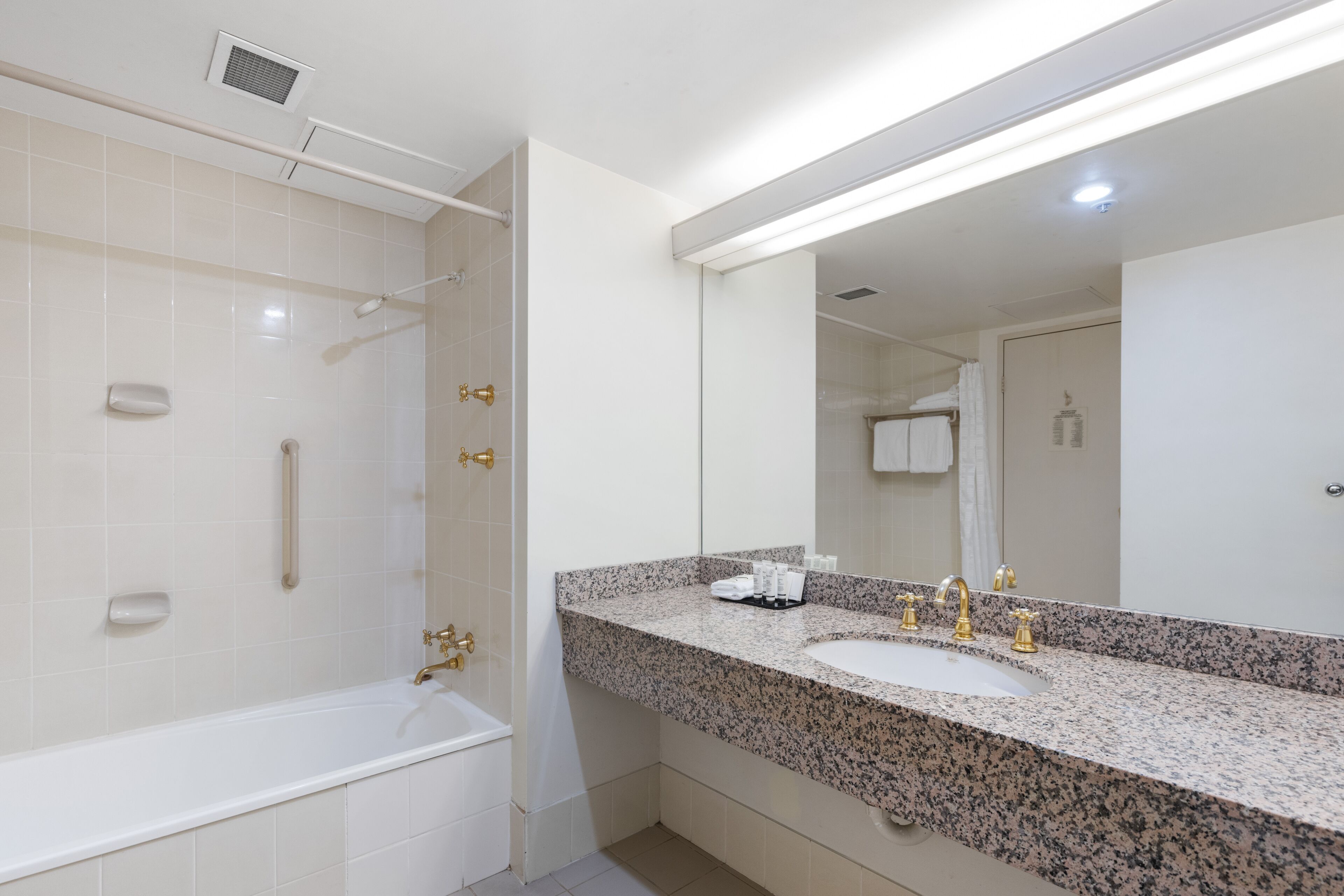 A modern bathroom with a white bathtub, a granite countertop sink, and a large mirror.