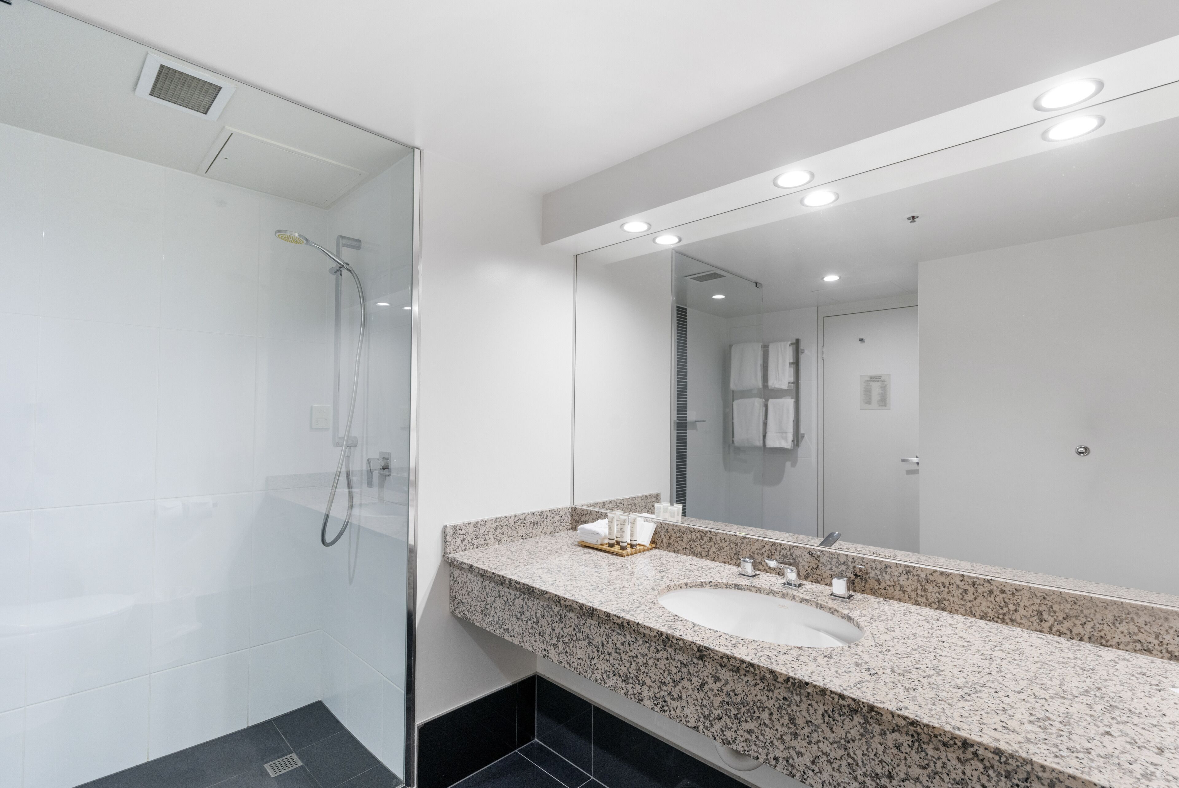 A modern bathroom with a glass-enclosed shower, a granite countertop sink, and a large mirror with integrated lighting.