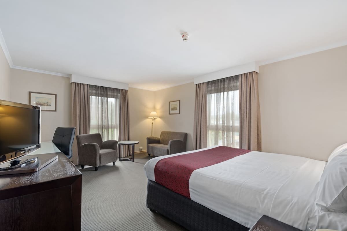 A hotel room with a bed, a desk with a TV, two armchairs, a small table, and a lamp.